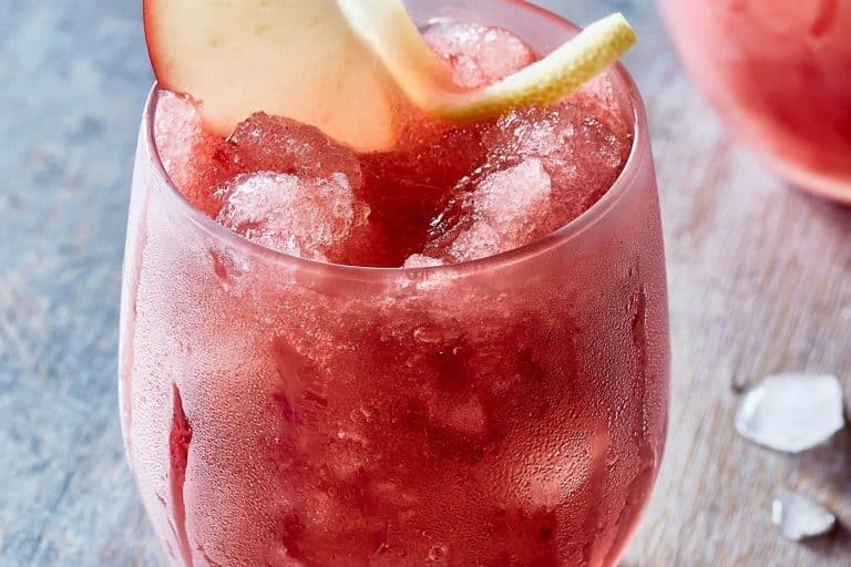 Un granité rose givré dans un grand verre avec une tranche de pomme et un zeste de citron