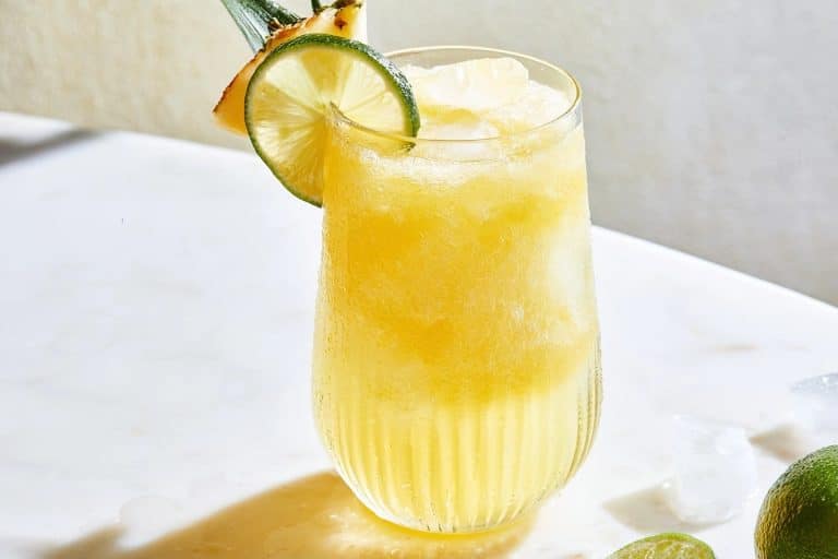 Slush jaune clair à l'ananas et au sureau dans un verre strié décoré de citron et d'ananas frais