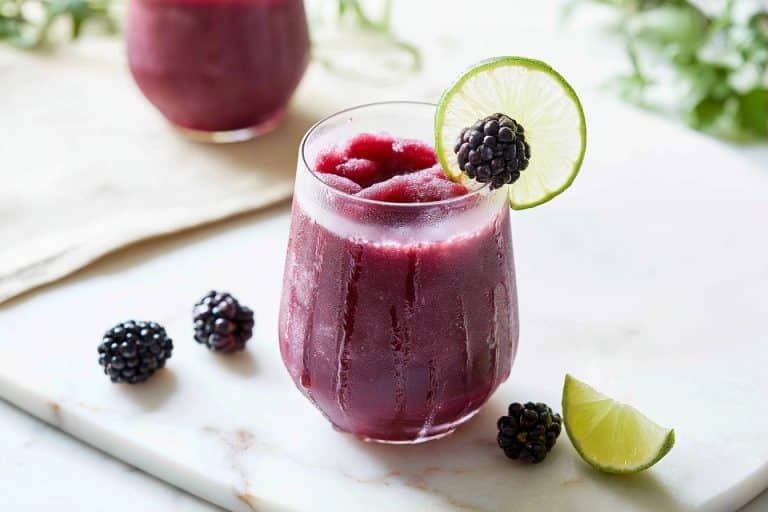 Un verre givré contient un granité violet aux mûres et citron vert, accompagné de fruits frais sur marbre