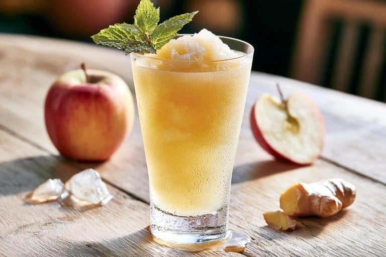 Un verre givré rempli d'un granité doré à la pomme et au gingembre avec menthe et fruits frais
