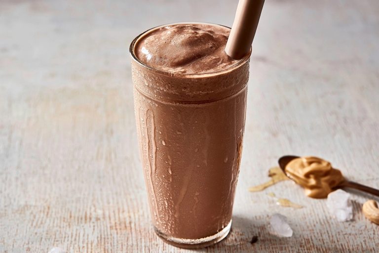 Un milkshake glacé au cacao et beurre de cacahuète dans un verre givré sur une table en bois